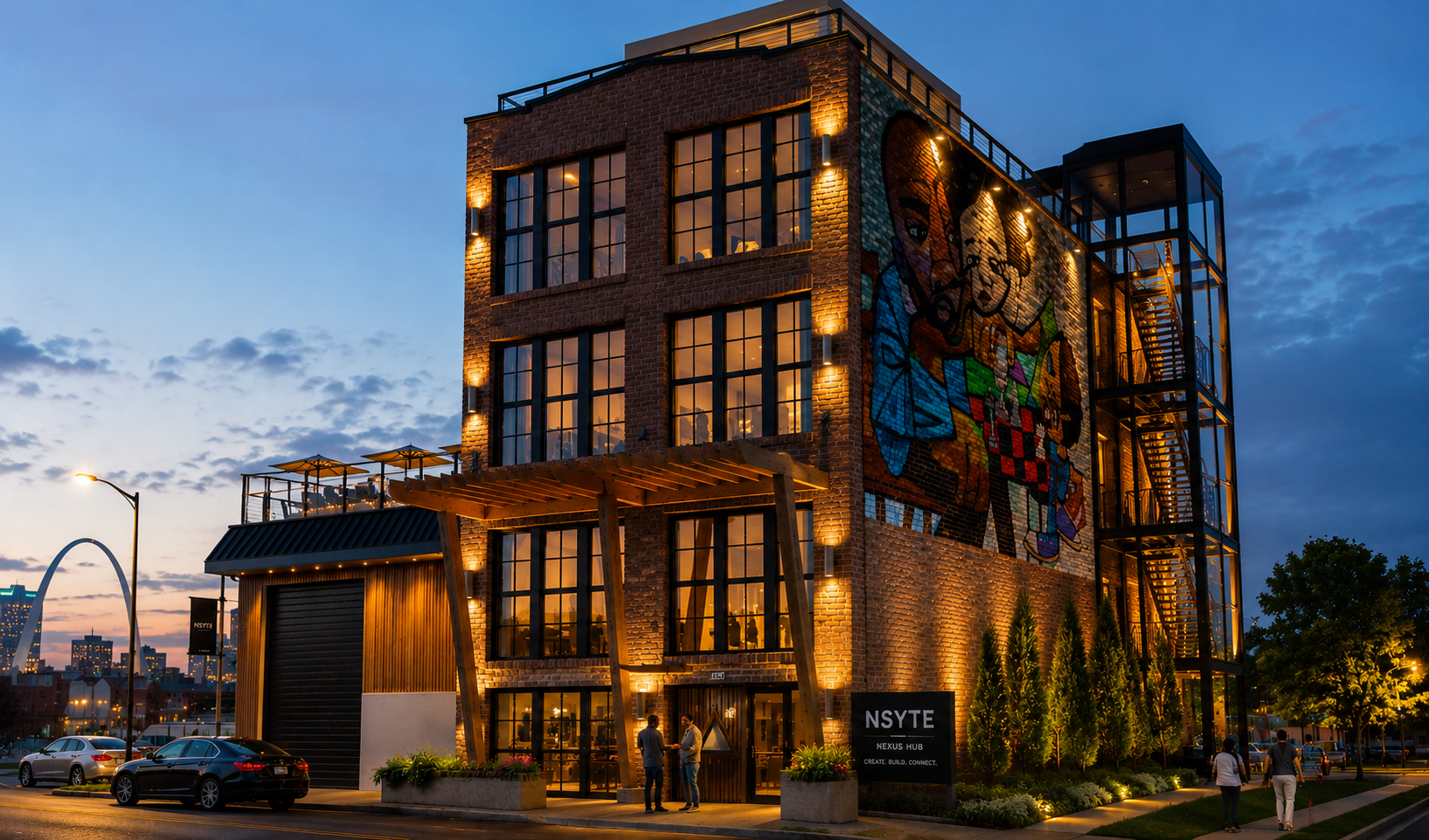The NSYTE compound at dusk. Restored brick facade with a large mural, warm façade lighting, and a lit street entrance in downtown St. Louis.